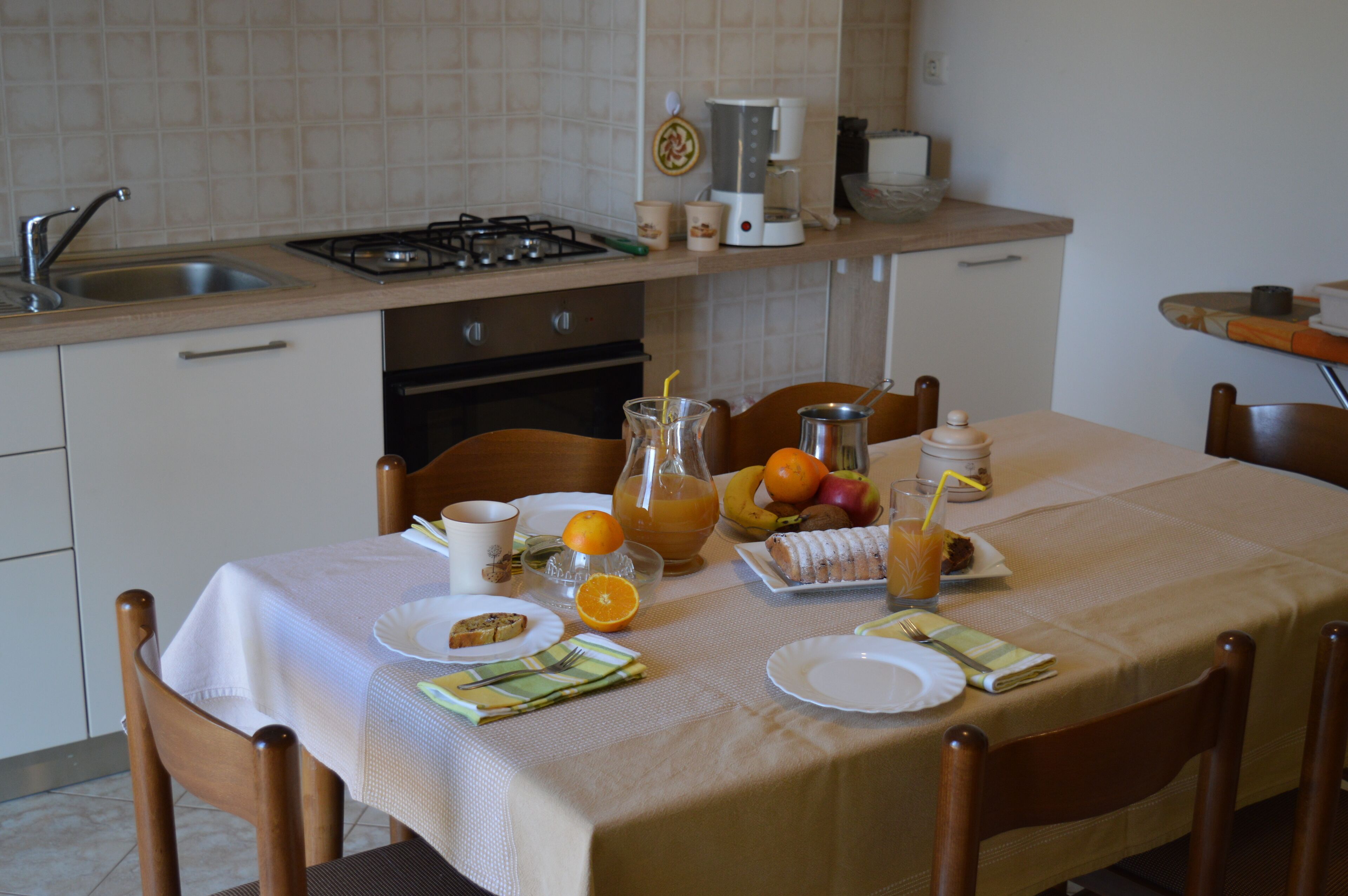 A kitchen with a dining table set for breakfast, including plates, cutlery, and a pitcher of orange juice.