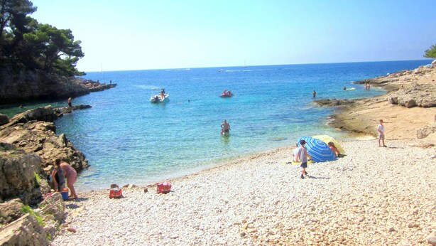 A pebble beach with clear blue water, rocky cliffs, and a few people enjoying the beach. - The apartment and free rental bikes, for families and active holidays (Pula)