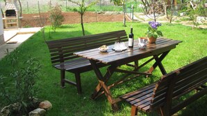 An outdoor patio with a wooden table and benches, surrounded by a well-maintained lawn and a brick oven. - The apartment and free rental bikes, for families and active holidays (Pula)