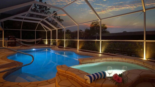 An indoor swimming pool with a glass ceiling, a hot tub, and a lounge area with a view of the sunset. - HD Smart TV's, Kayaks, Pool & Spa, WIFI, Gulf Access, E-Dart Board, Bar, Grill  (Cape Coral)
