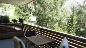 A balcony with a wooden table and chairs, overlooking a mountainous landscape with trees. - 6 min from the center and the MatterhornParadise station, next to the ski bus stop (Zermatt)