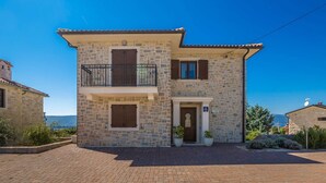A two-story stone house with a balcony, a door with a glass panel, and potted plants at the entrance. - Villa LURDA with a magnificent sea view and heated pool (Linardići)