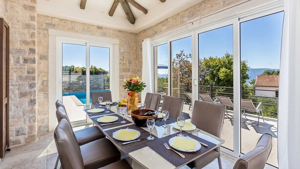 A dining area with a table set for four, large windows, and a view of the sea. - Villa LURDA with a magnificent sea view and heated pool (Linardići)