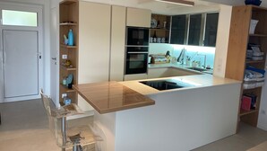 A modern kitchen with a central island, built-in oven, and wooden shelves.