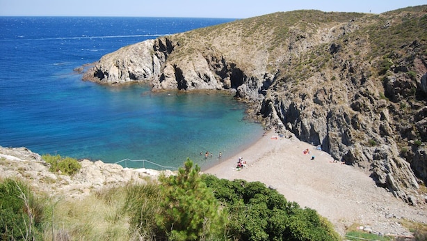 A rocky coastline with a beach and clear blue sea.