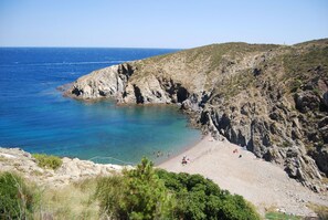 Eine Küstenlandschaft mit felsigem Strand, klarem blauem Meer und hügeligem Gelände.