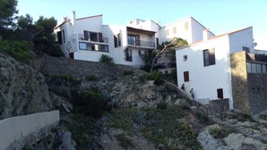 A hillside property with white buildings, a stone retaining wall, and a rocky terrain.