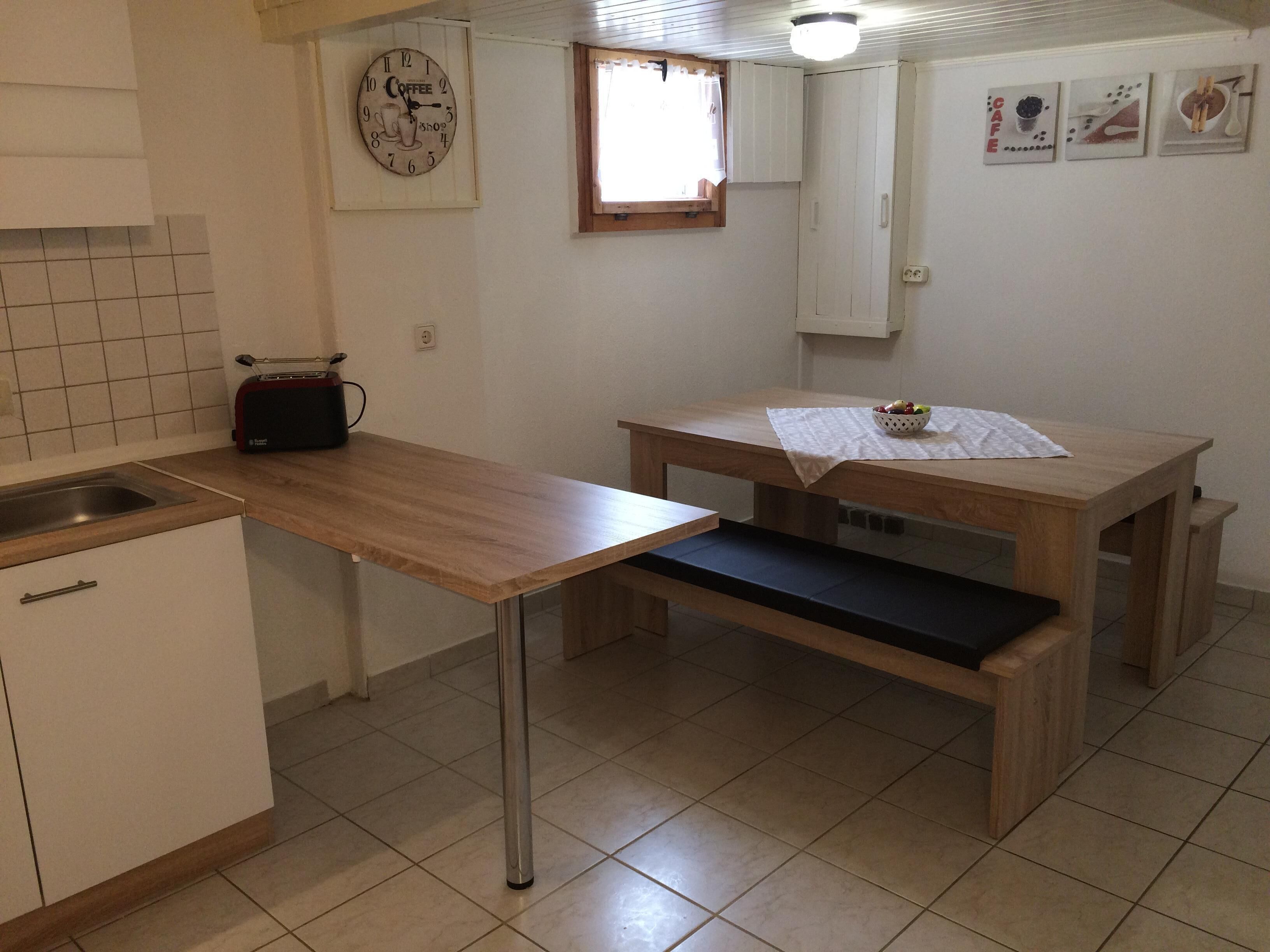 A small kitchen with a wooden countertop, a sink, a coffee-themed wall clock, and a window with curtains.