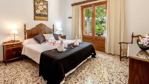 A bedroom with a bed, wooden headboard, bedside tables, a nightstand, a desk, a chair, a window with curtains, and a painting on the wall. - Holiday house with pool, air conditioning in the bedrooms, internet / outside kitchen with barbecue, (Pollensa)