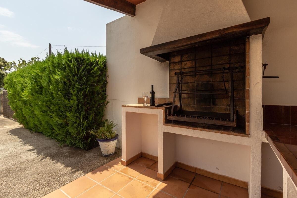 An outdoor grill area with a stone fireplace, a potted plant, and a tiled patio.
