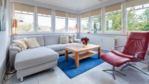 A modern living room with a sofa, a red chair, a wooden coffee table, and large windows with blinds. - Flooded with light, close to the center, WLAN, 400 m z. Beach (Zingst)