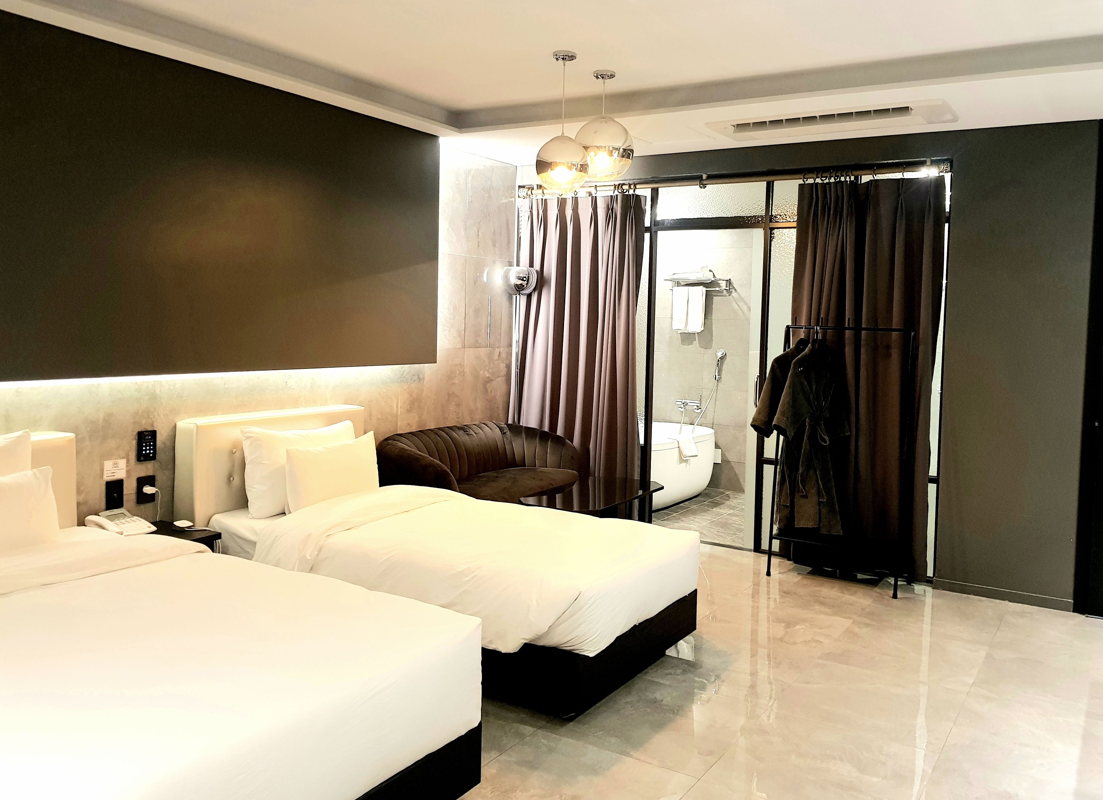 A modern hotel room with two beds, a bathroom with a bathtub, and a robe rack.