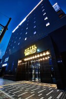 Un hôtel moderne, reconnaissable à son grand panneau « HÔTEL RECHERCHÉ », à ses larges portes d’entrée en verre et à son hall d’entrée carrelé.