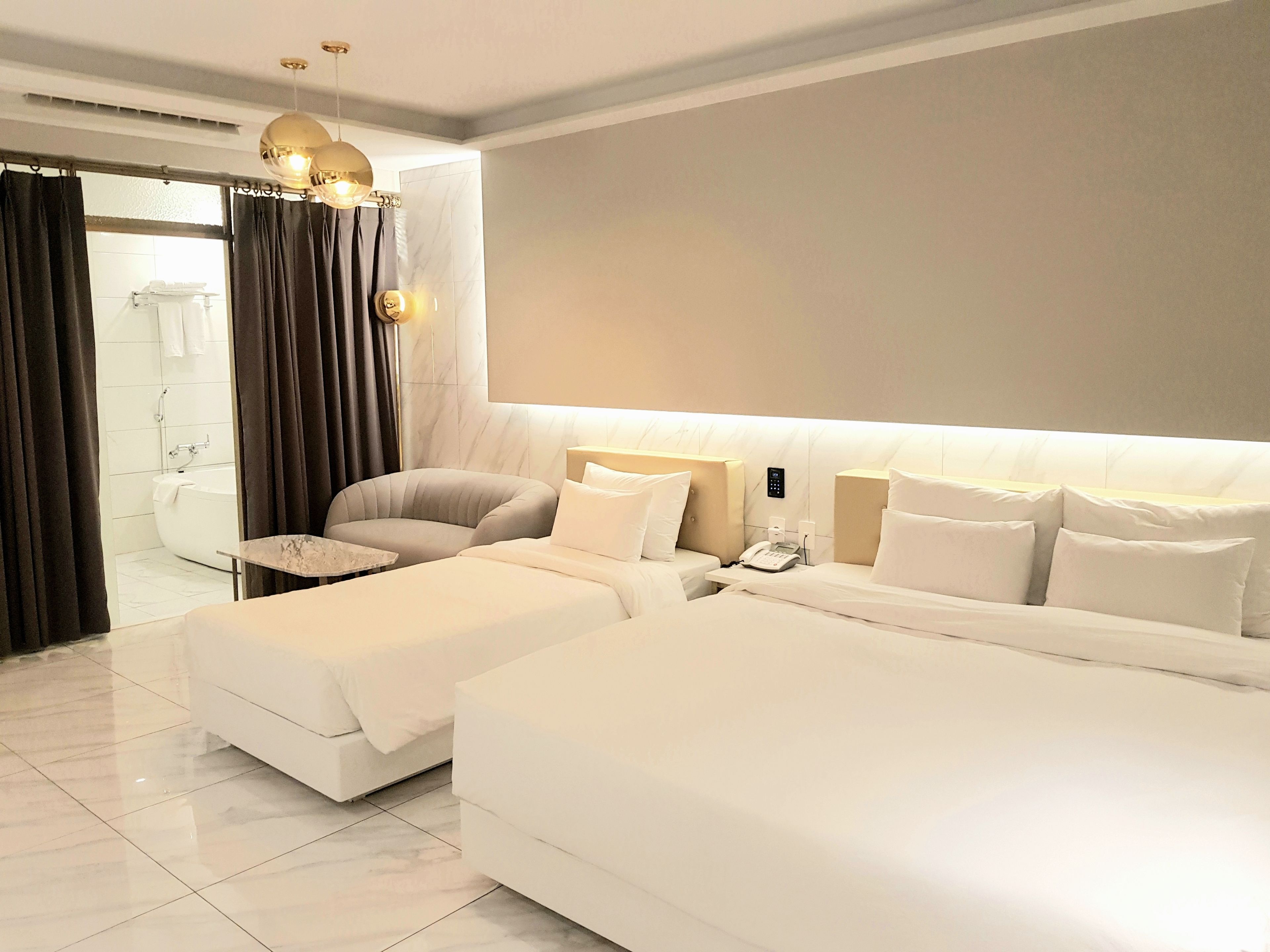 A modern hotel room with a large bed, a smaller sofa, a desk, and a bathroom visible through an open door.