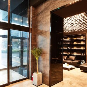 A modern lobby with a glass wall, a potted plant, a bookshelf, and a seating area. - Hotel Wanted (Incheon)