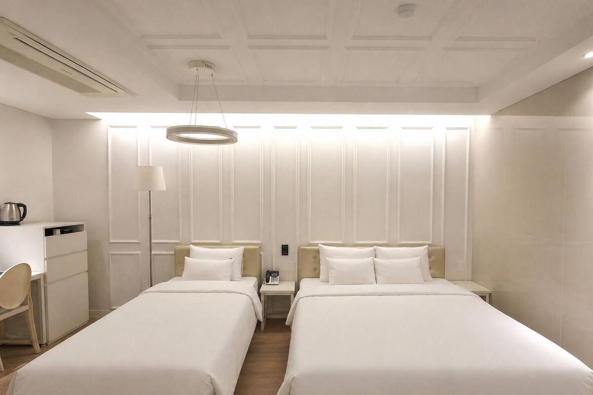 Une chambre d’hôtel avec deux lits, un bureau, une lampe et un luminaire au plafond.