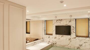 Un baño moderno con pared de mármol, bañera empotrada y un televisor de pantalla plana sobre la bañera.