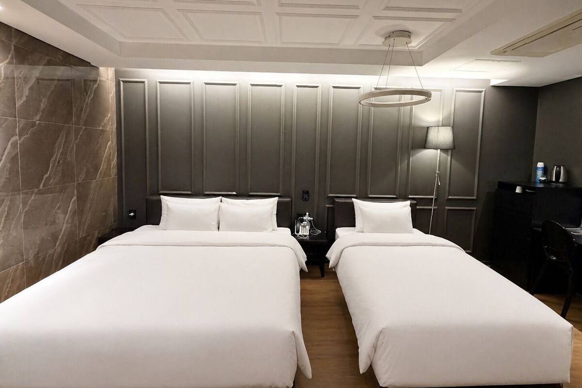 Une chambre d’hôtel avec deux lits, un bureau, une lampe et un mini-bar.