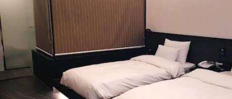 Una habitación de hotel con dos camas, un armario de madera y un escritorio pequeño con teléfono.