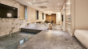 Quarto de hotel moderno com casa de banho em mármore, área de estar com sofá e cadeiras, e mesa de jantar.