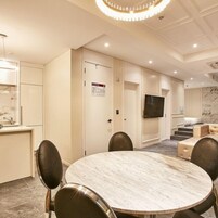 Une chambre d’hôtel moderne dotée d’une table à manger en marbre, de sièges confortables, d’un téléviseur à écran plat et d’un escalier menant à un balcon.