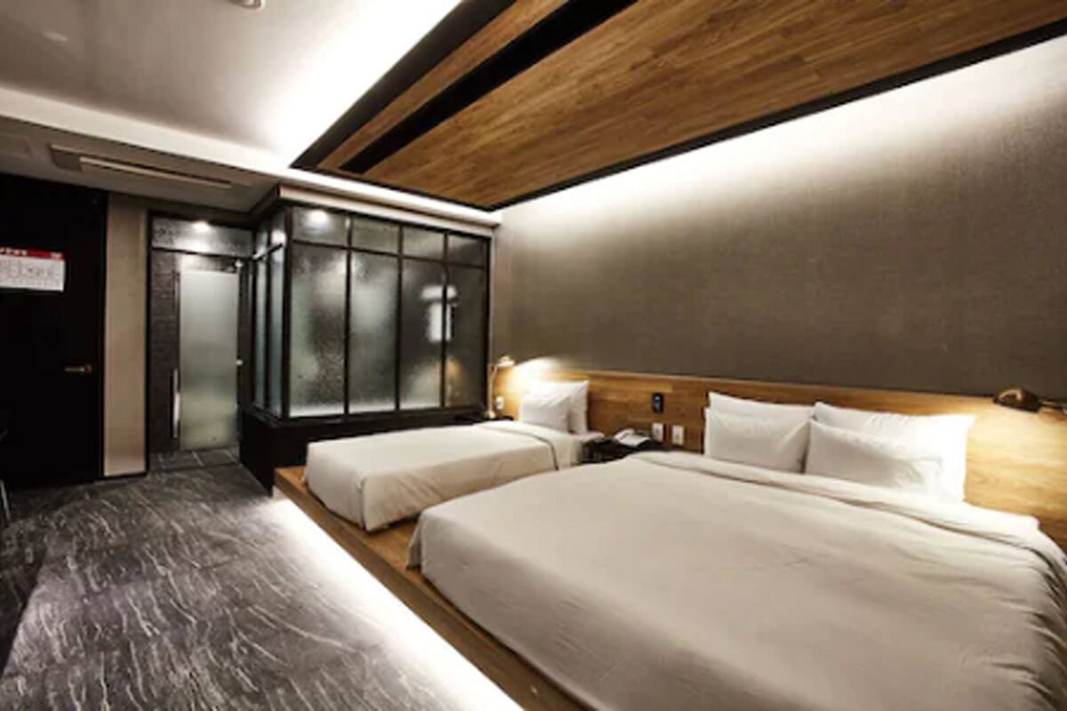 Une chambre d’hôtel avec deux lits, une tête de lit en bois, une armoire intégrée et un sol en marbre.