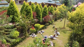 A resort with multiple buildings, a well-maintained garden with various trees, and a children's play area with ride-on toys. - Nature Bloom Dharamshala Hotel and Resort (Palampur)