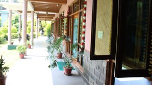 A covered outdoor area with potted plants, a wooden ceiling, and a stone wall. - Nature Bloom Dharamshala Hotel and Resort (Palampur)