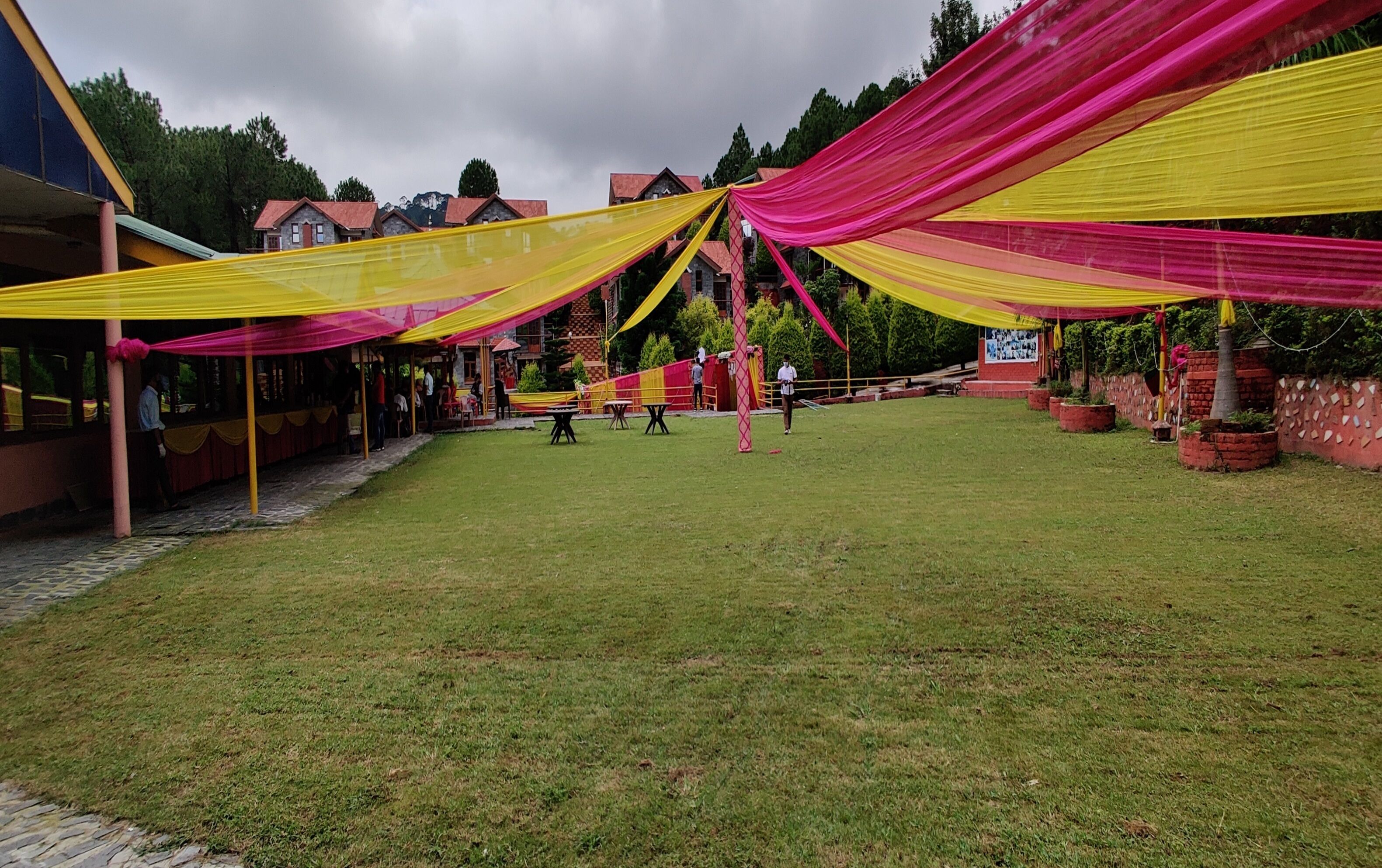 An outdoor area with a grassy lawn, a building with a red roof, and a structure with yellow and pink drapes.