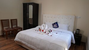 A neatly made bed with white bedding, two wooden chairs, a wardrobe, and a bedside table with a kettle. - Nature Bloom Dharamshala Hotel and Resort (Palampur)