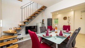 A dining area with a table set for four, a staircase, and a television. - Holiday house MICHAEL with shared pool and private jacuzzi (Pinezići)