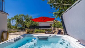 A hot tub with a red umbrella, surrounded by a stone wall and greenery. - Holiday house MICHAEL with shared pool and private jacuzzi (Pinezići)