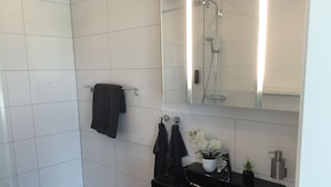 Een moderne badkamer met witte tegels, een zwarte wastafel, een spiegel en een douche.