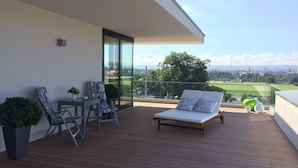 Een balkon met houten vloer, een lounge stoel, een tafel met stoelen en een schilderij.