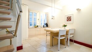 Een keuken met een houten tafel en stoelen, een raam met gordijnen en een trap.