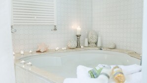 Een badkamer met een groot bad, witte honingraat tegels, een brandende kaars en toiletartikelen op de rand.