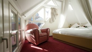 Een slaapkamer met een rood tapijt, een bed, een roze stoel en een raam met gordijnen.