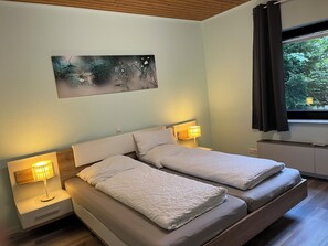 A double bed with two bedside tables, each with a lamp, in a room with a window and a painting on the wall.