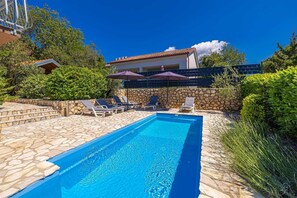 Une piscine entourée de murs de pierre et de verdure, avec des chaises longues et des parasols.