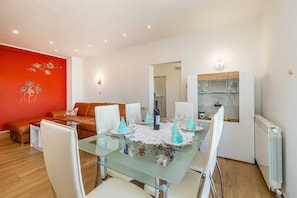 Een eethoek met een glazen tafel, witte stoelen en een rode accentmuur.