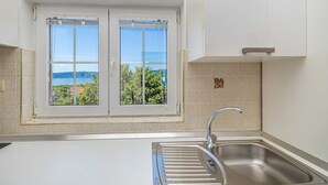 A kitchen with a double window, a stainless steel sink, and a view of the sea. - Apartment JENNY 1 with pool and sea view (Pinezici)