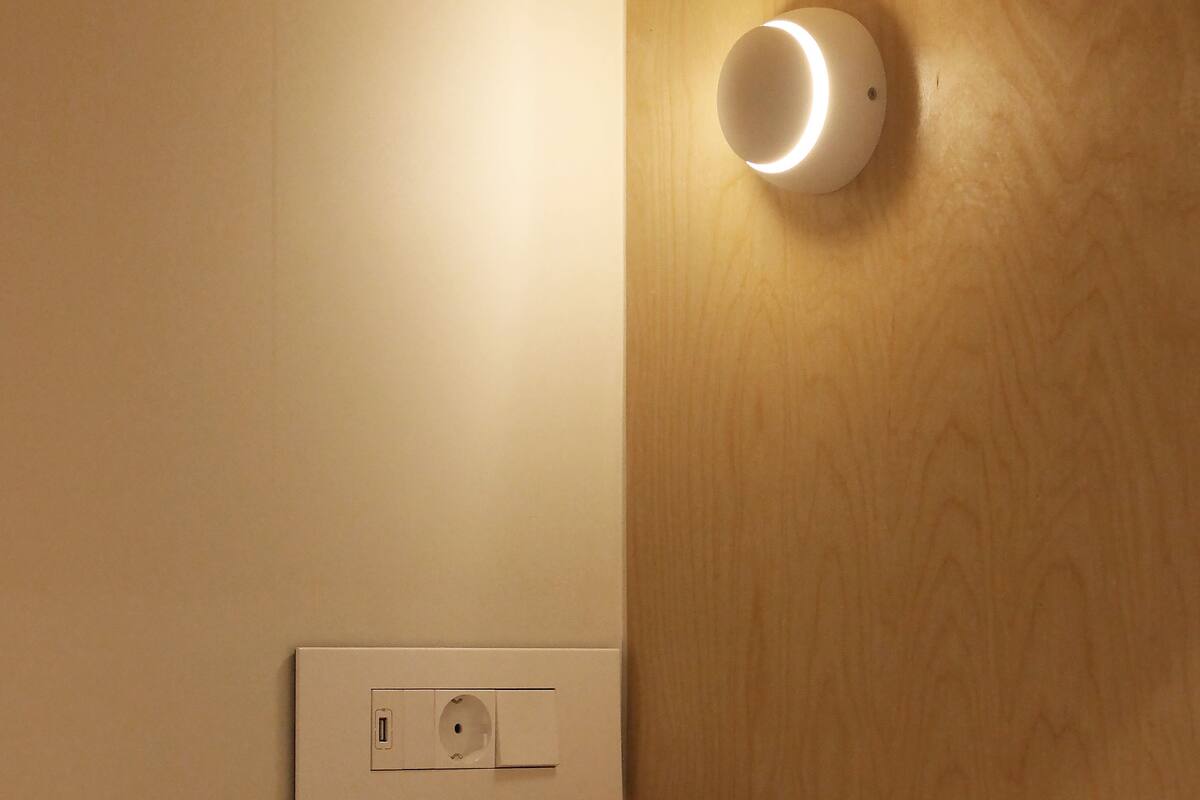Een hotelkamer met een houten hoofdbord, een nachtkastje, een wit kussen en een wandlamp.