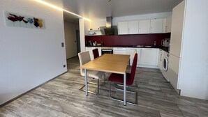 Une cuisine moderne avec des meubles blancs, une table à manger en bois et une chaise rouge.