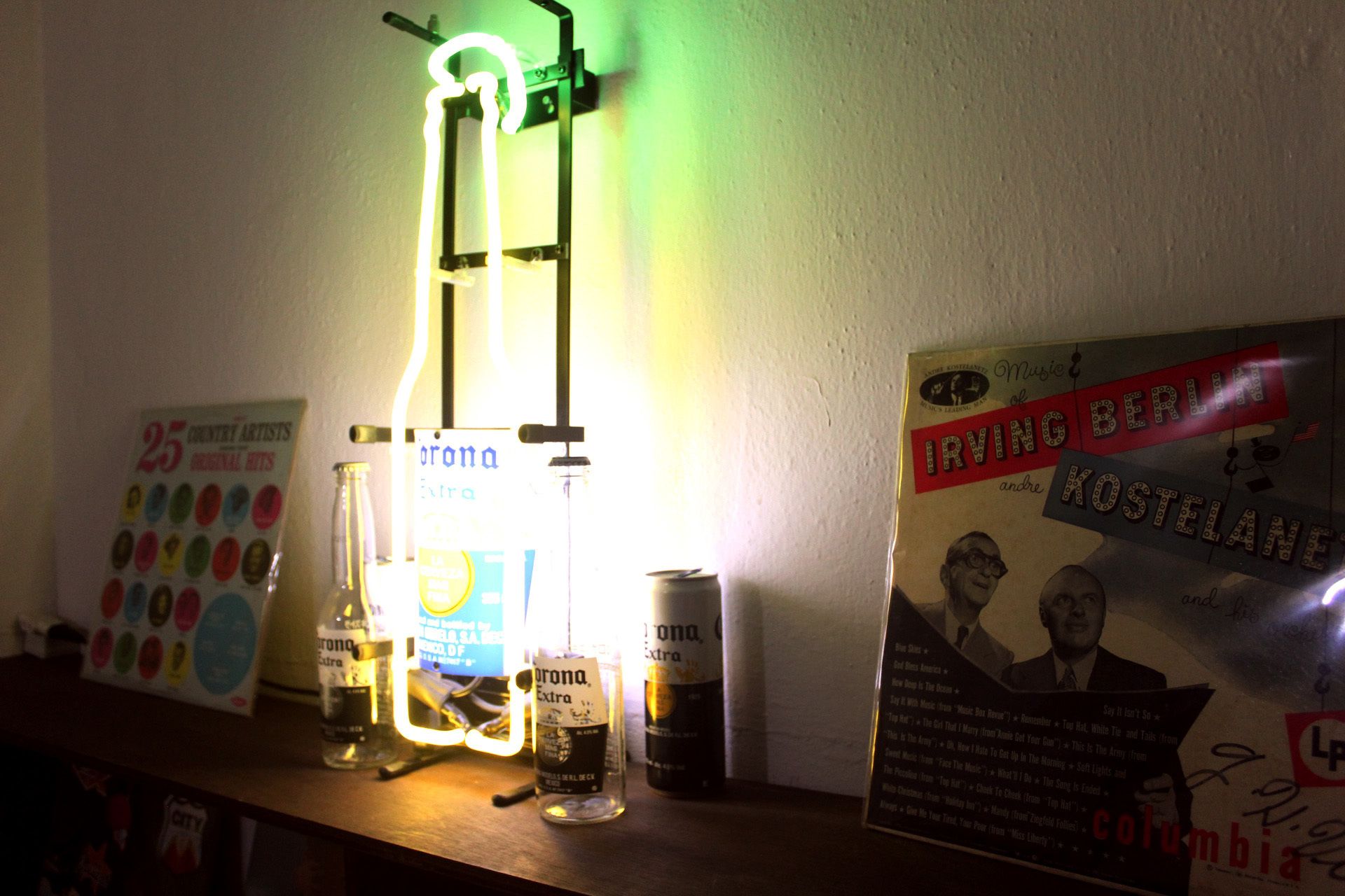 Una estantería con botellas de cerveza Corona Extra, un letrero de neón y un cartel de Irving Berlin.