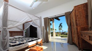 A bedroom with a bed, a wooden bench, a ceiling fan, and a view of the outdoors. - Authentic Beachvilla with cook, private pool, staff and lush tropical garden (Seririt)