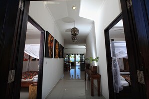 A hallway leading to a bedroom with a bed, a bedside table with a plant, and a large window with a view. - Authentic Beachvilla with cook, private pool, staff and lush tropical garden (Seririt)
