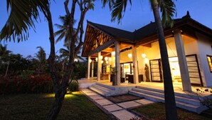 A modern house with a covered porch, palm trees, and a well-lit entrance. - Authentic Beachvilla with cook, private pool, staff and lush tropical garden (Seririt)