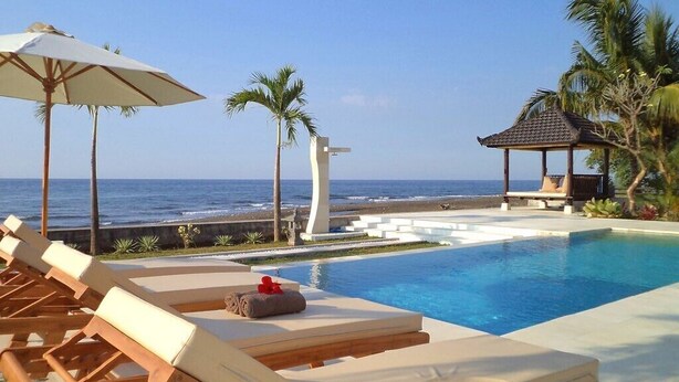 A poolside area with lounge chairs, a small gazebo, and a view of the ocean. - Authentic Beachvilla with cook, private pool, staff and lush tropical garden (Seririt)