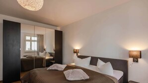 Habitación de hotel moderna con una cama grande, mesitas de noche, un espejo y vistas al exterior.