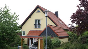 A two-story house with a red-tiled roof, a covered driveway, and a car parked in the driveway.